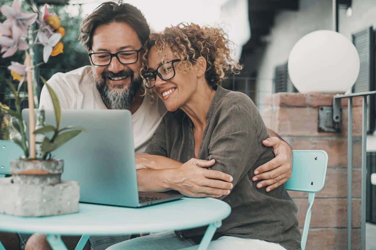 Happy-couple-laptop-smiling Happy couple hugging smiling at laptop