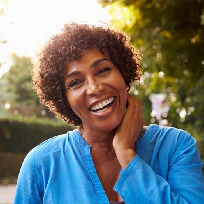 Smiling-woman-new -smile-dentures-teeth-happy-outside Smiling woman outdoors wearing blue