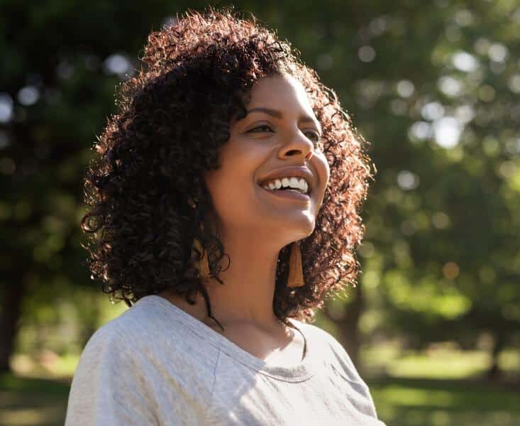 Woman-smiling-outside-healthy-teeth Black woman smiling outdoors beautiful teeth